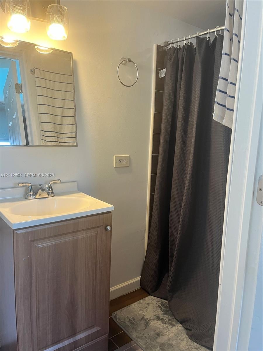 Bathroom featuring a wood-finish vanity with a rectangular sink, chrome dual-handle faucet, rectangular wall-mounted mirror, and tiled shower surround