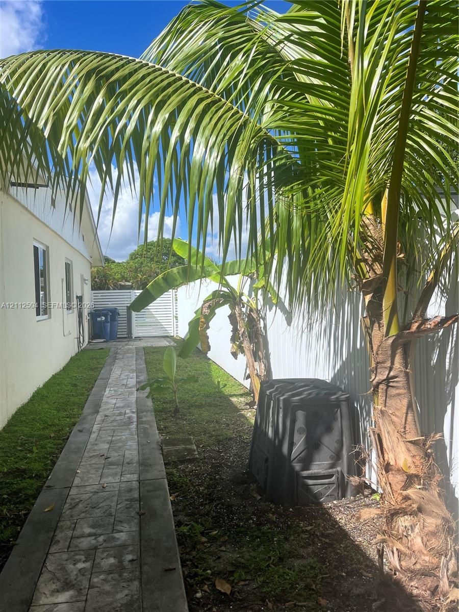 Side yard featuring a concrete paver walkway, white privacy fencing, and mature palm vegetation