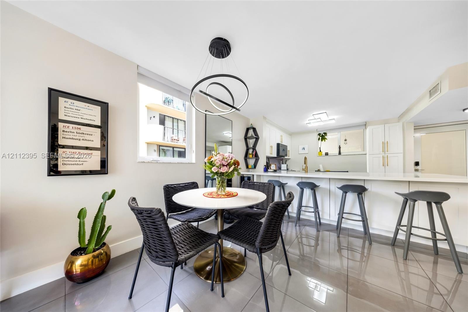 Open-concept kitchen and dining area featuring large-format tile flooring, white cabinetry with gold-tone hardware, a breakfast bar, and a modern tier