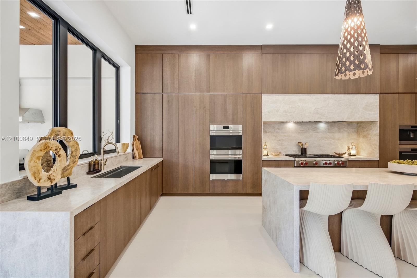 Kitchen featuring flat-panel wood-finish cabinetry, stone countertops with waterfall edge, integrated stainless steel double wall oven, and geometric 