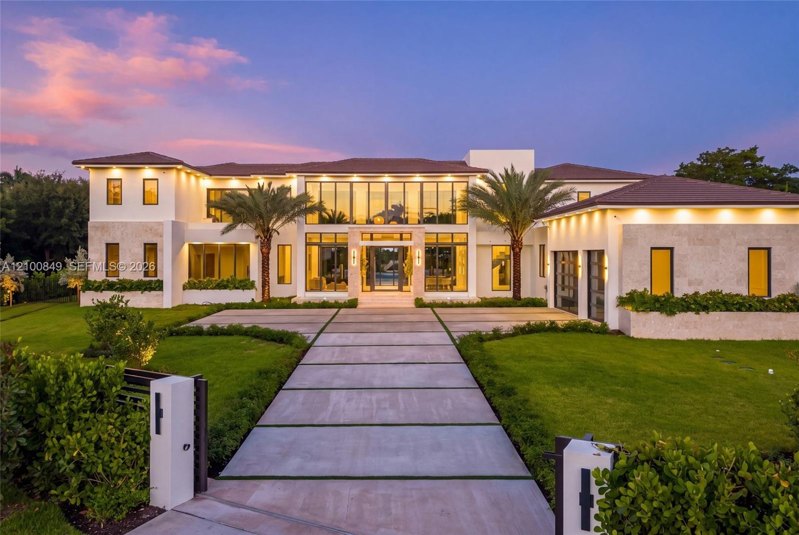 Two-story modern residence featuring stone-clad exterior walls, expansive floor-to-ceiling glass windows, a structured concrete paver driveway, and pr