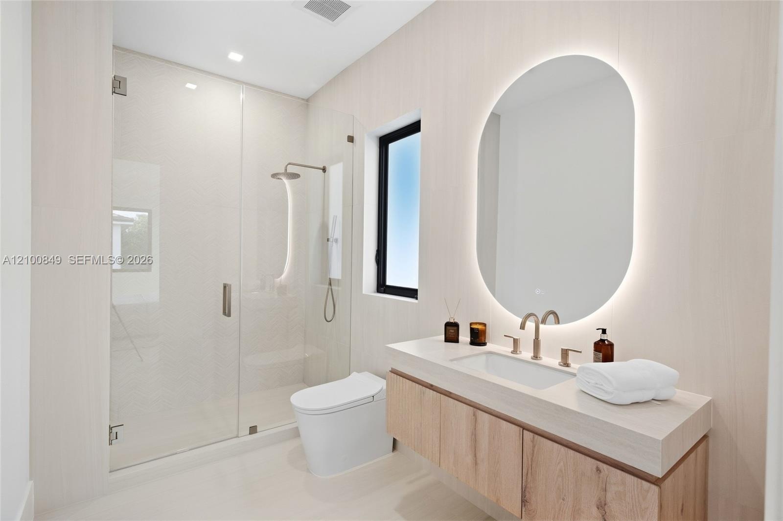 Floating vanity featuring a wood-finish cabinet and integrated countertop, complemented by an oval-shaped LED backlit mirror