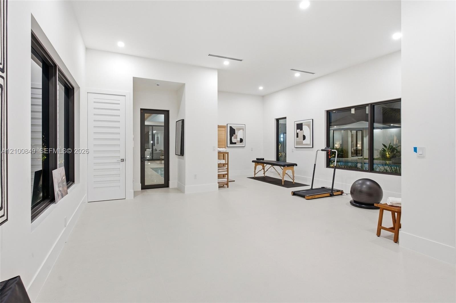 Spacious interior featuring high ceilings, recessed lighting, large windows with dark frames, smooth-finish flooring, and a glass-paneled door
