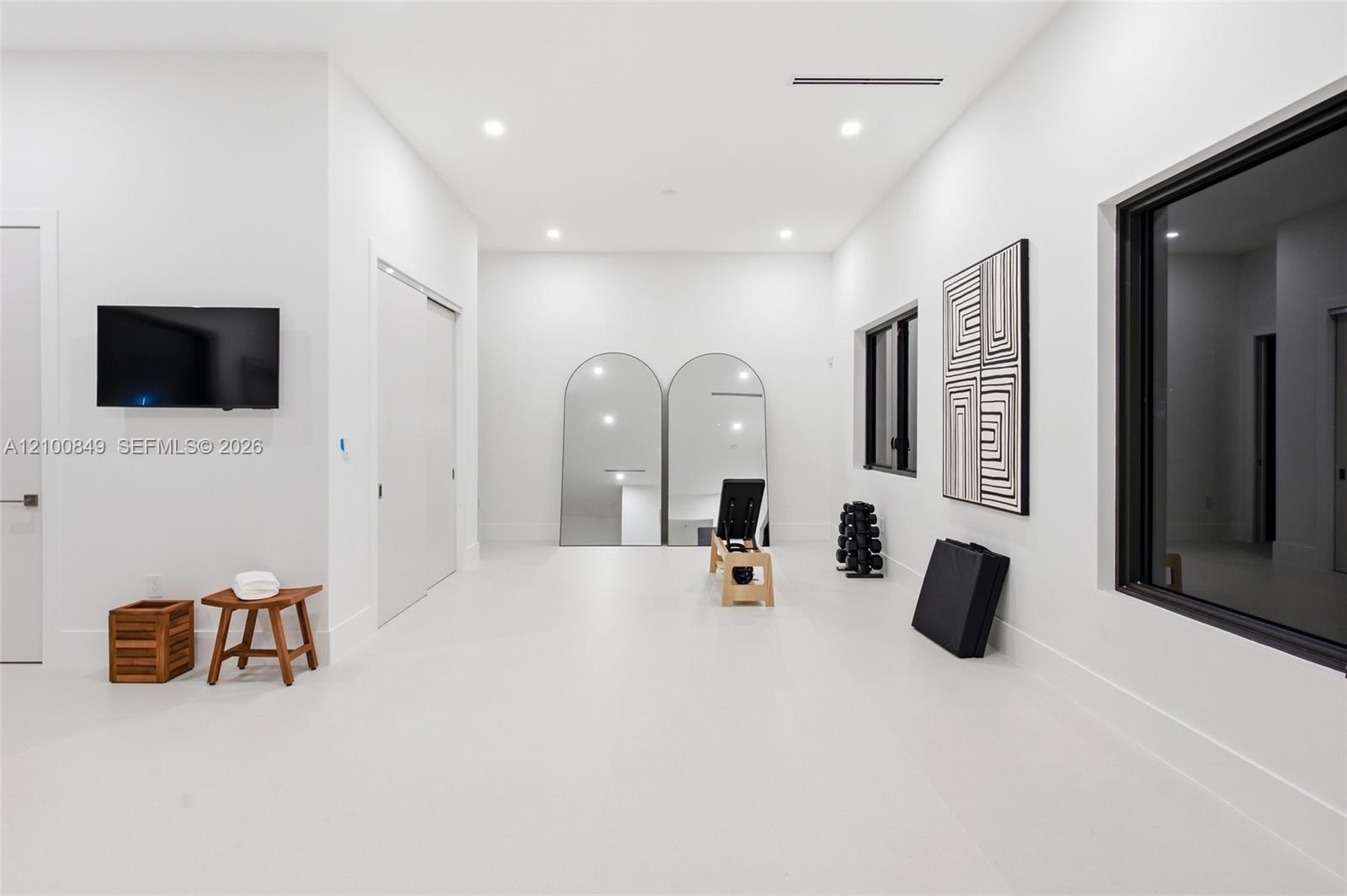 Spacious room featuring high ceilings, recessed lighting, smooth-finish solid flooring, and multiple large windows with dark trim