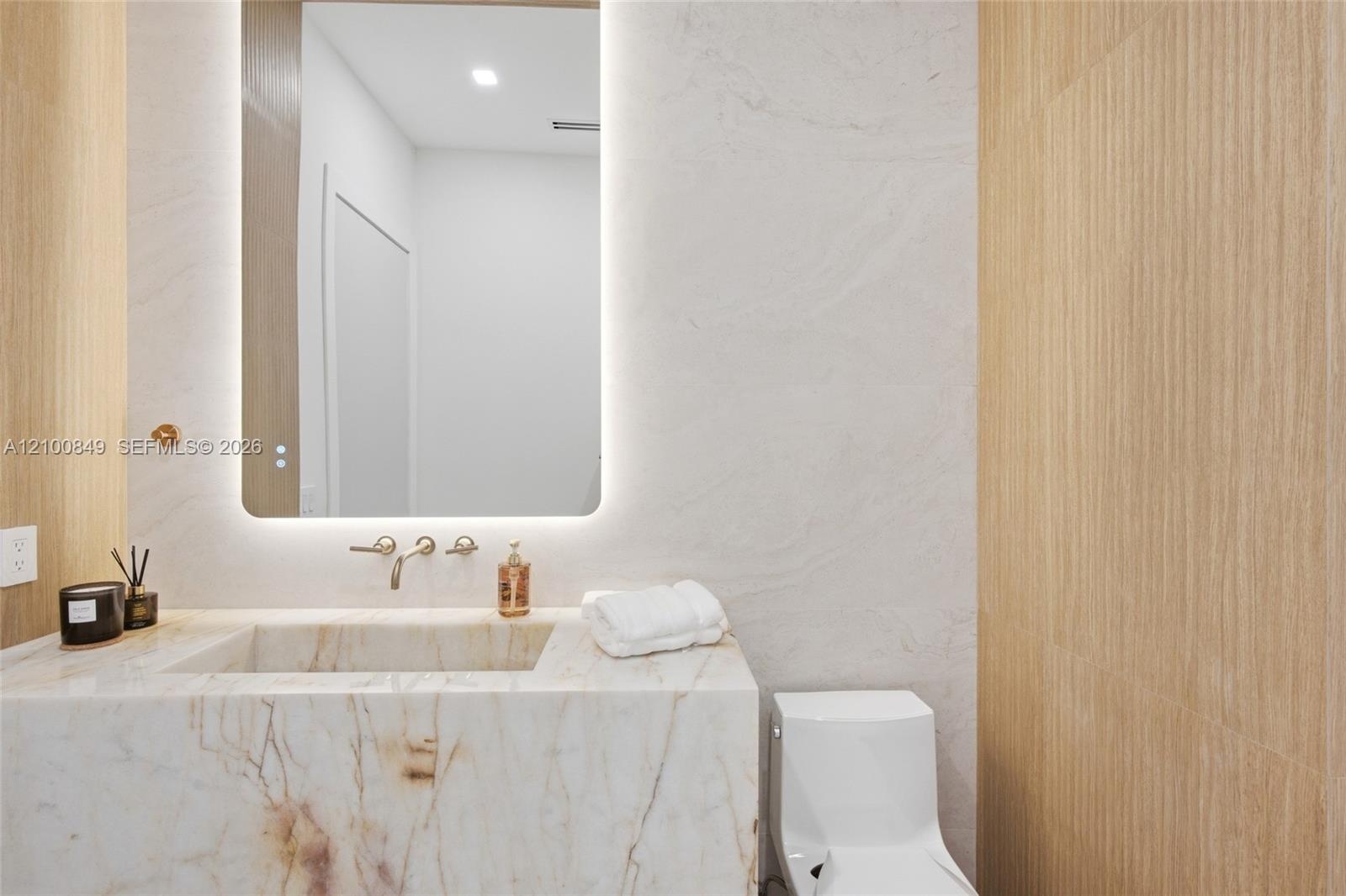 Stone-clad integrated vanity with a seamless basin, wall-mounted faucet, backlit rounded mirror, and wood-finish wall paneling