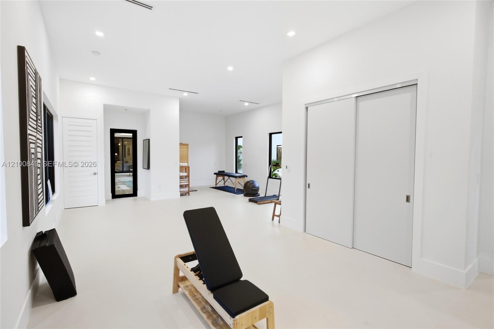 Spacious room featuring high ceilings, recessed lighting, matte-finish light-toned flooring, sliding double closet doors, and black-framed windows
