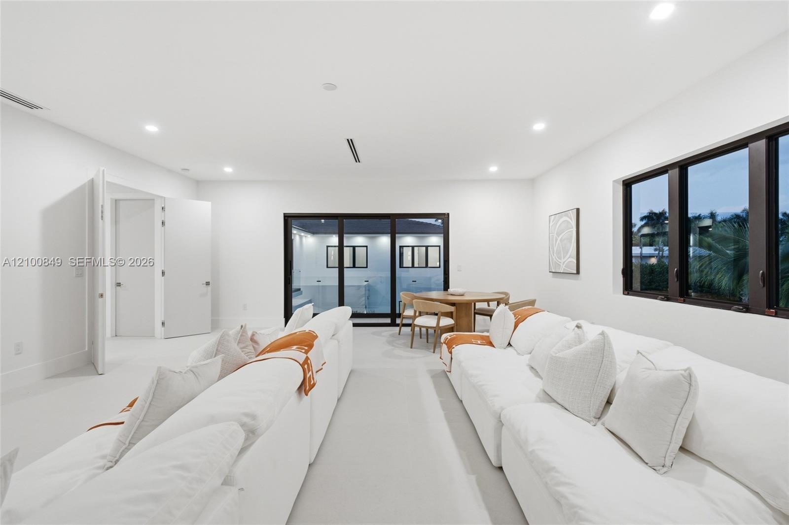 Open-concept interior featuring recessed ceiling lighting, smooth-finish flooring, multi-panel sliding glass doors with dark frames, and large horizon