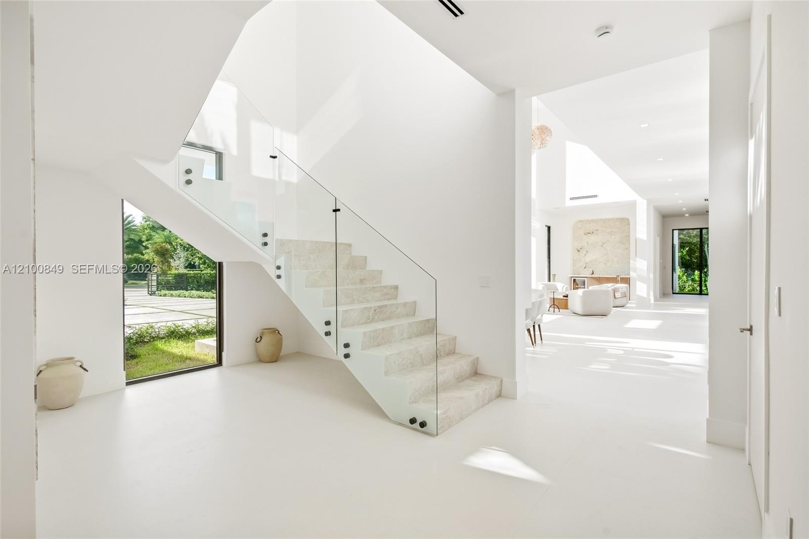 Open-riser staircase with stone treads and frameless glass railing, polished stone flooring, and expansive windows