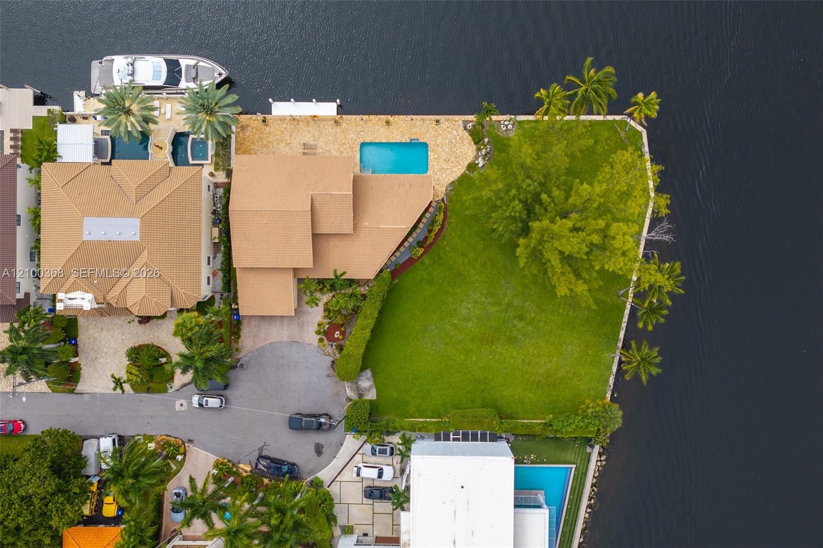 Waterfront property featuring a wraparound seawall, swimming pool with paved decking, extensive lawn, and mature perimeter landscaping