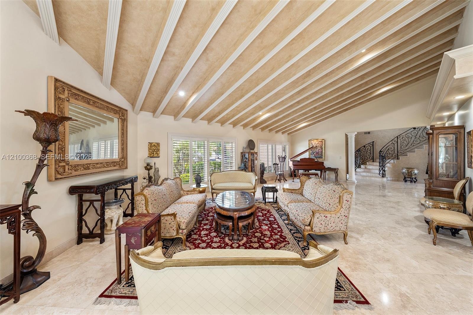 Vaulted ceiling with decorative wood beams, stone flooring, recessed lighting, and ornate staircase with decorative metal railing