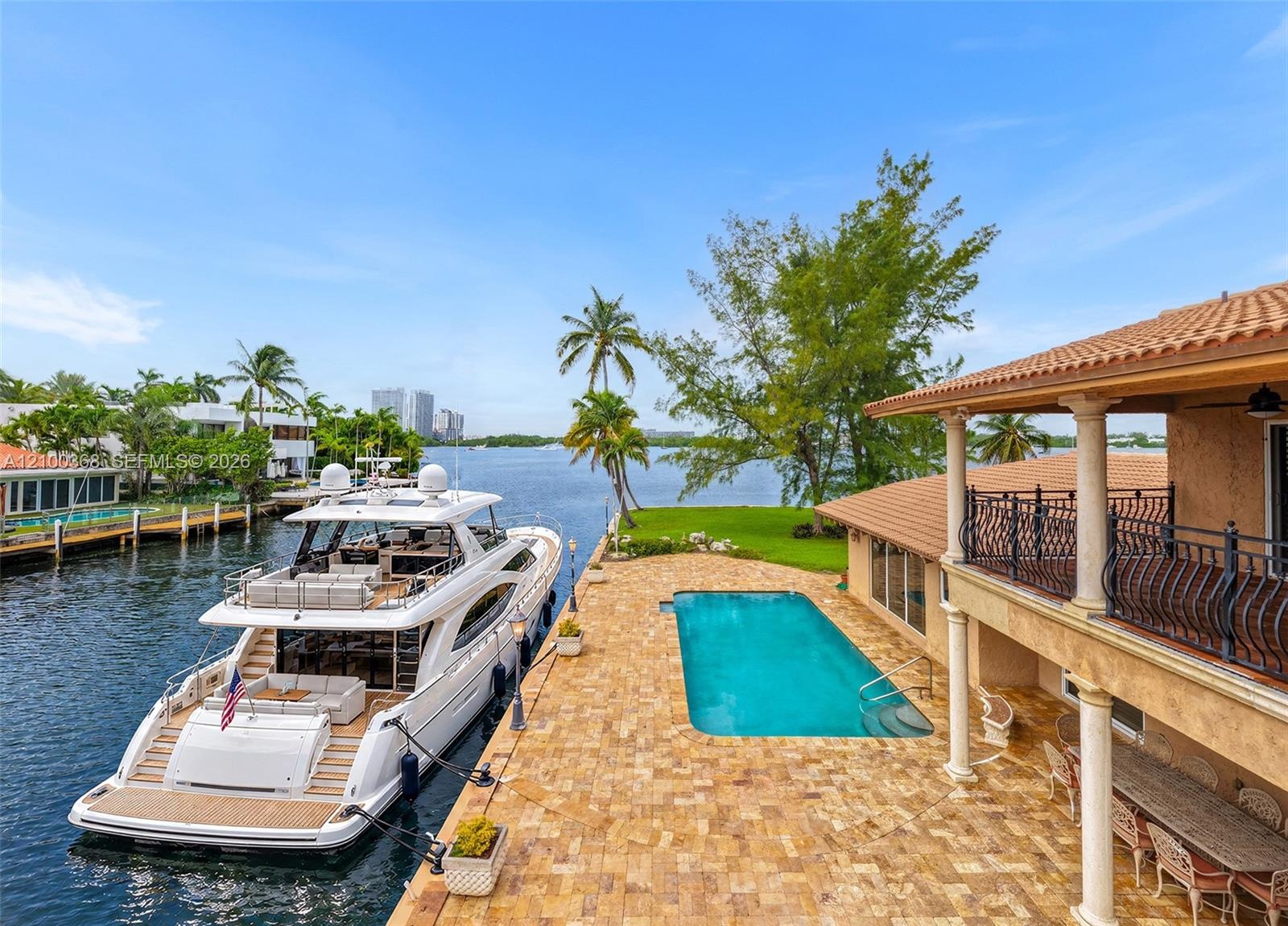 Waterfront estate featuring a private boat slip, rectangular swimming pool, stone-paver patio, covered porch with classical columns, and an upper-leve