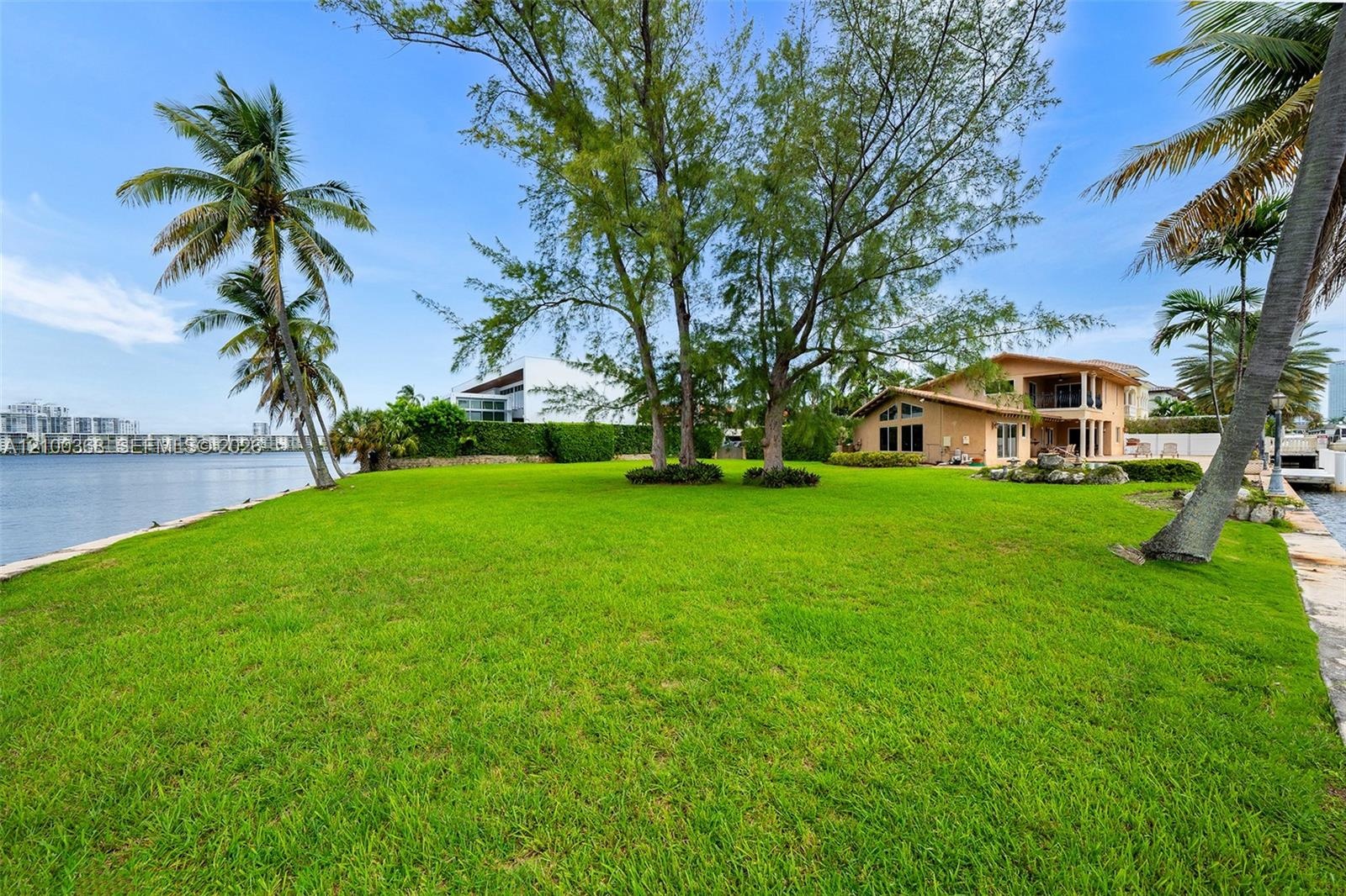 Expansive waterfront property featuring a manicured lawn, mature trees, palm trees, and direct water frontage