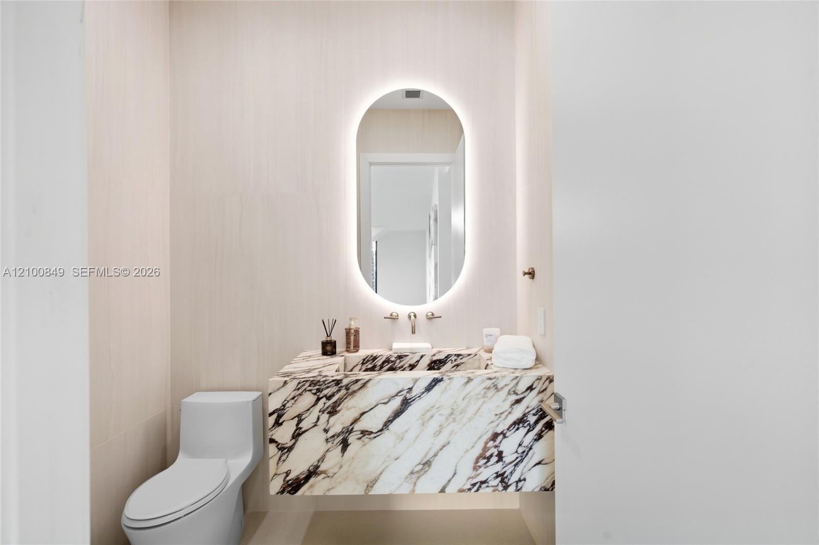 Modern powder room featuring a sculptural oval illuminated mirror with integrated lighting, elegant veined stone vanity countertop with waterfall edge