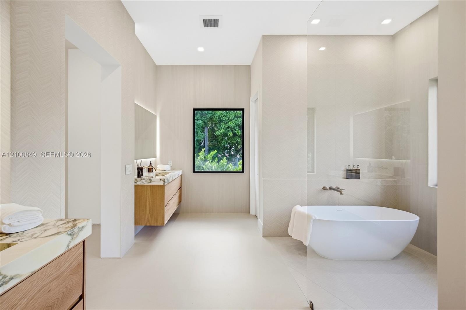 Bathroom featuring a floating wood-finish double vanity, integrated stone countertop, freestanding soaking tub, glass-enclosed wet area, and recessed 