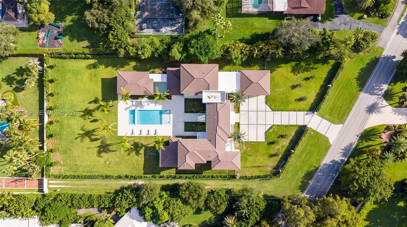 Aerial perspective featuring a multi-wing residence, expansive manicured lawn, paved driveway with geometric grid patterns, and an integrated swimming