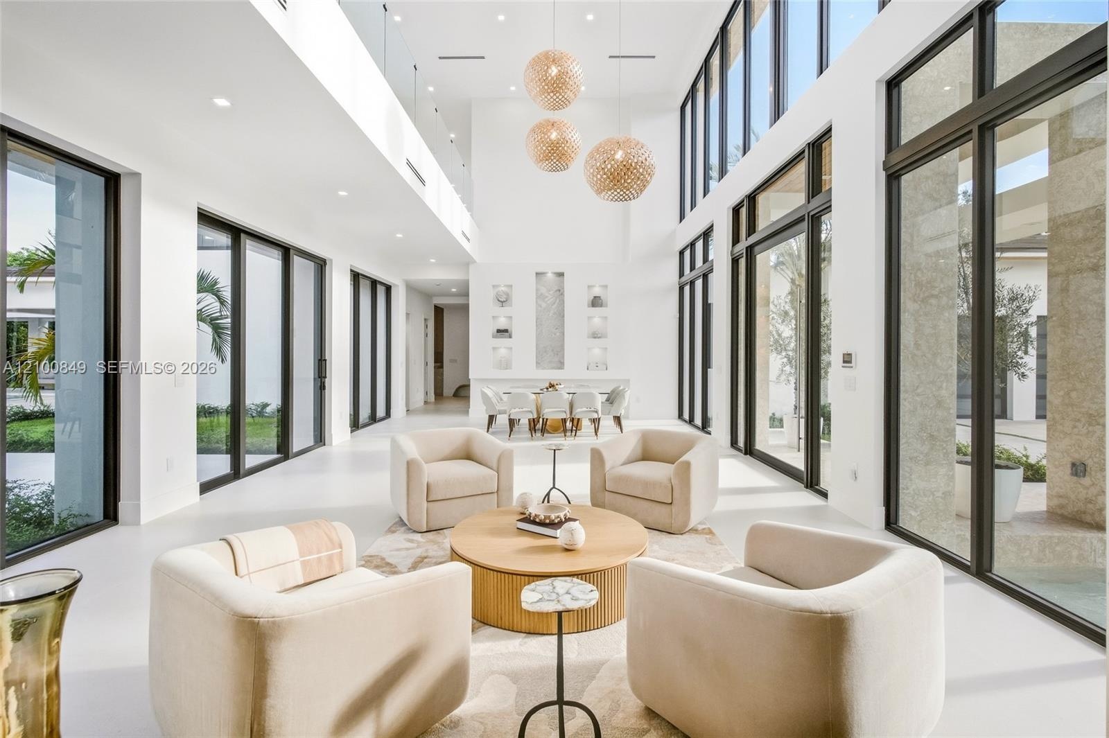 Double-height ceilings, floor-to-ceiling black-framed windows, multi-tiered orb pendant lighting, glass-paneled mezzanine railing, and integrated wall