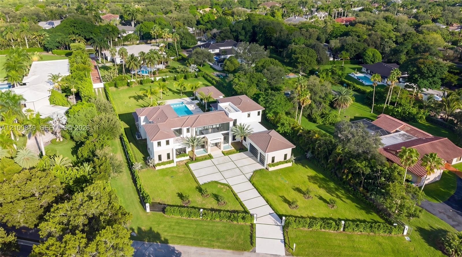 Aerial perspective of a multi-story residence featuring a tile roof, an expansive manicured lawn, a gated motor court, and a swimming pool