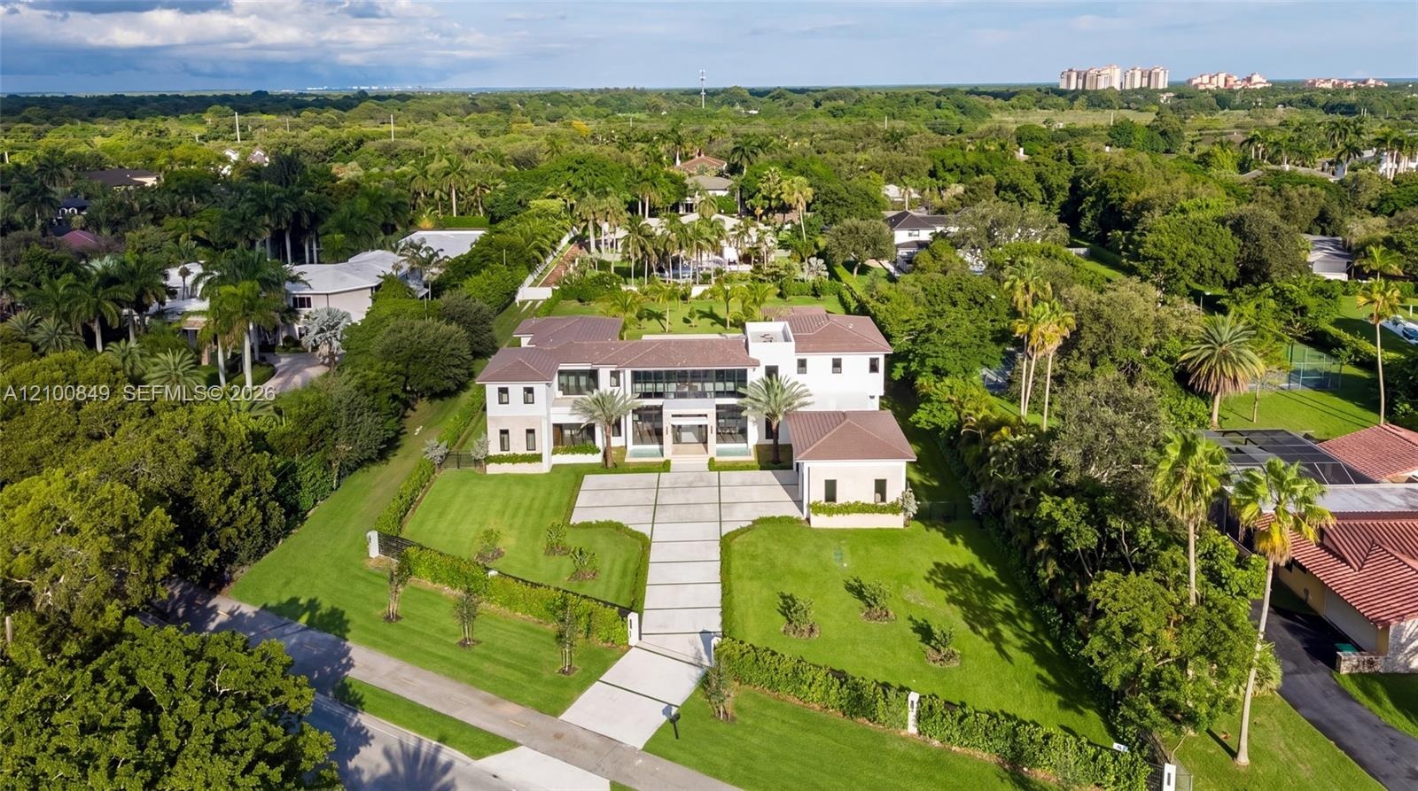 Two-story estate featuring a light-colored stucco exterior, multi-hipped tile roof, extensive lawn area, paved motor court, and mature palm landscapin