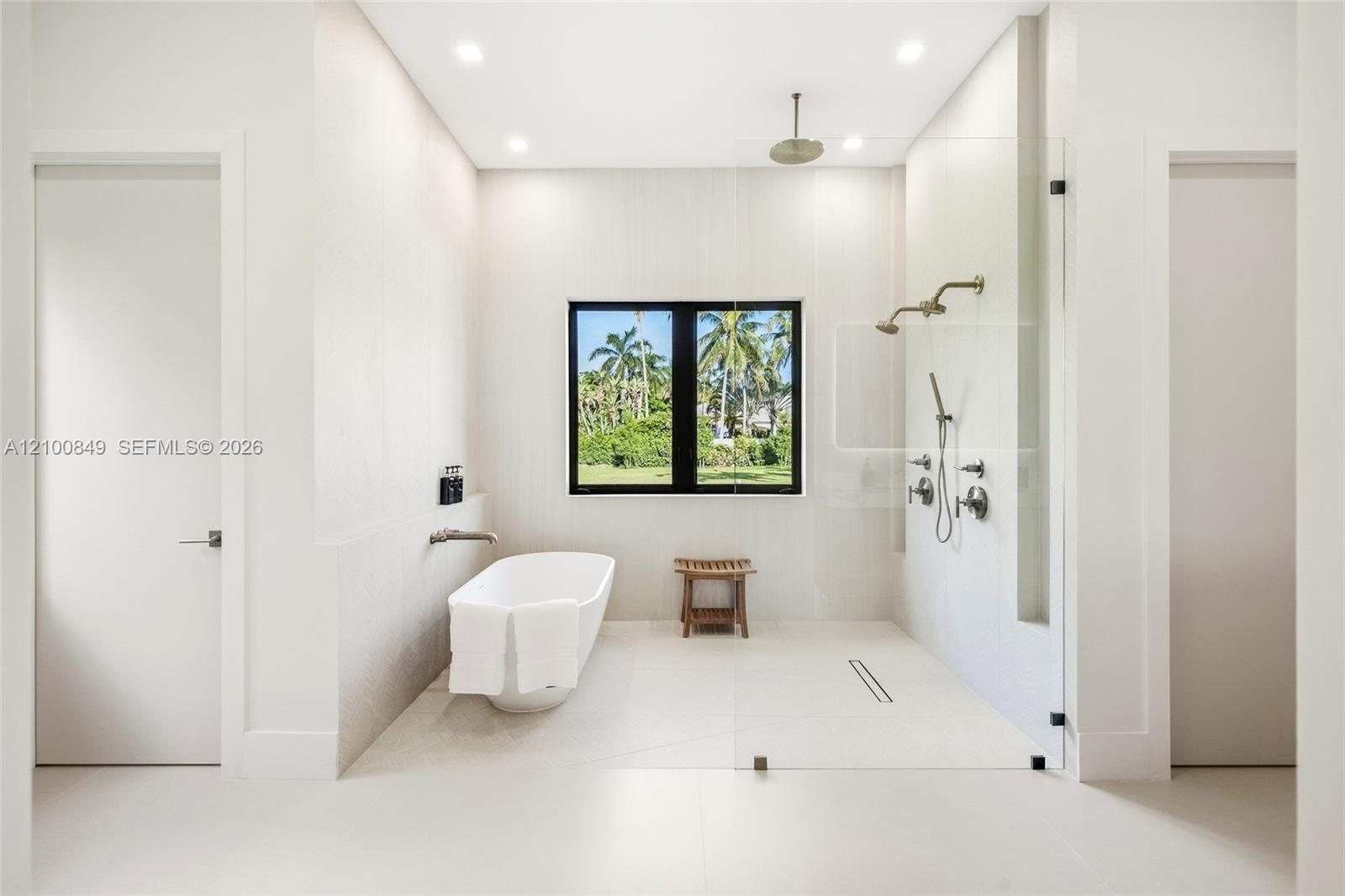 Freestanding soaking tub with wall-mounted faucet, walk-in shower with glass enclosure, dual shower heads, and large-format tile flooring