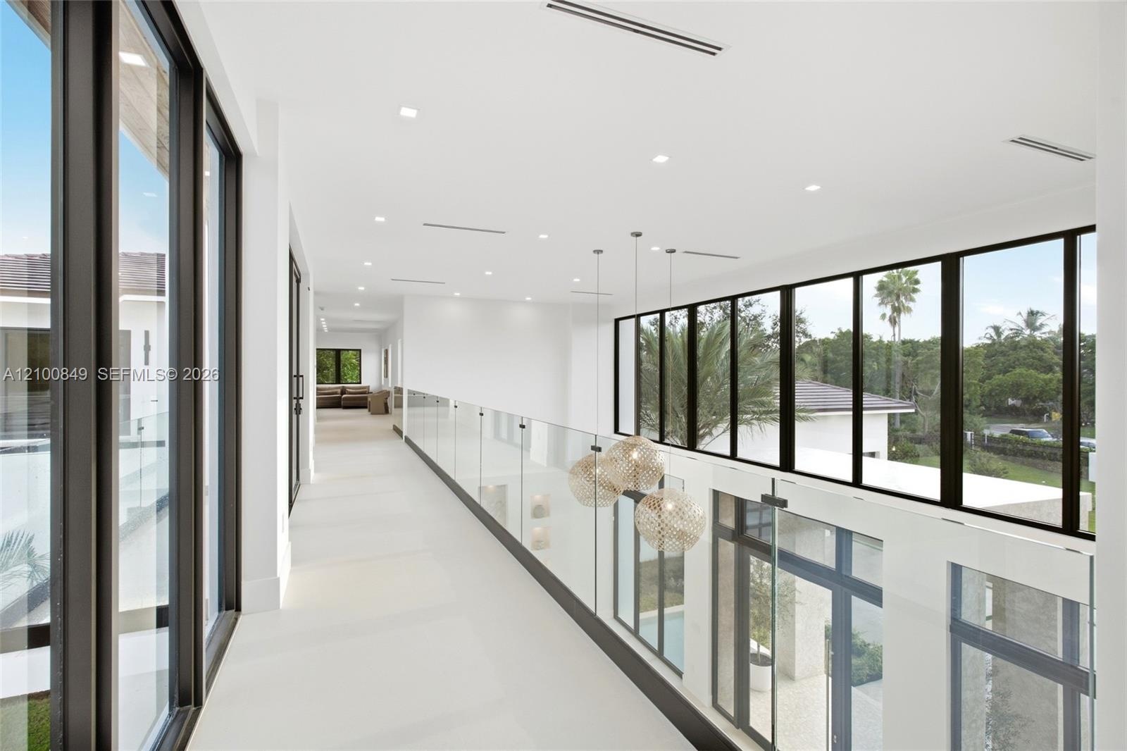 Hallway featuring floor-to-ceiling black-framed windows, frameless glass railings, recessed lighting, and integrated globe-style pendant fixtures