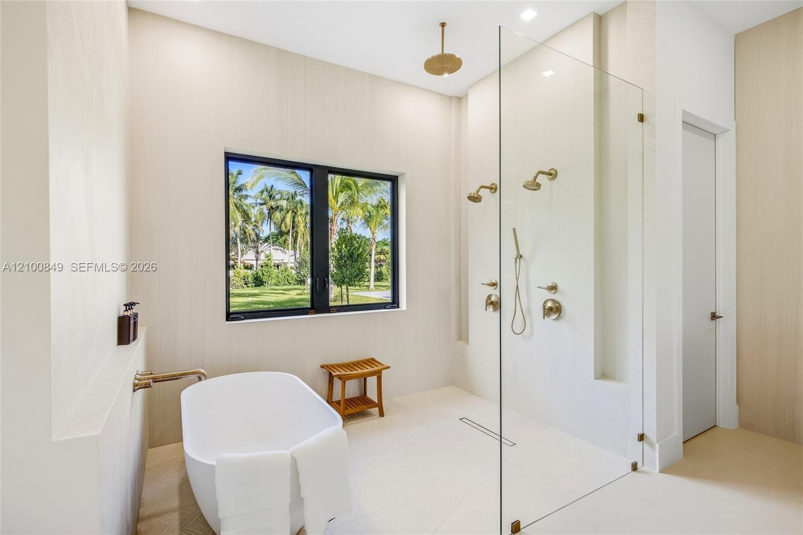 Freestanding soaking tub with wall-mounted faucet, walk-in shower featuring a frameless glass enclosure, gold-toned rainfall and handheld showerheads,