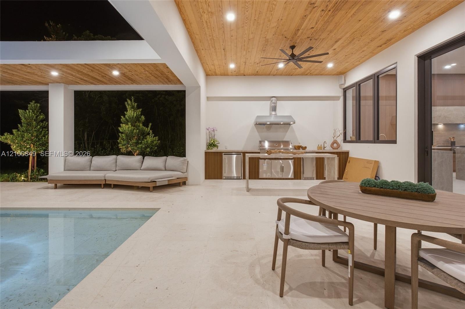Covered outdoor kitchen featuring built-in cabinetry, stainless steel appliances, and a ventilation hood, complemented by a wood-plank ceiling, recess