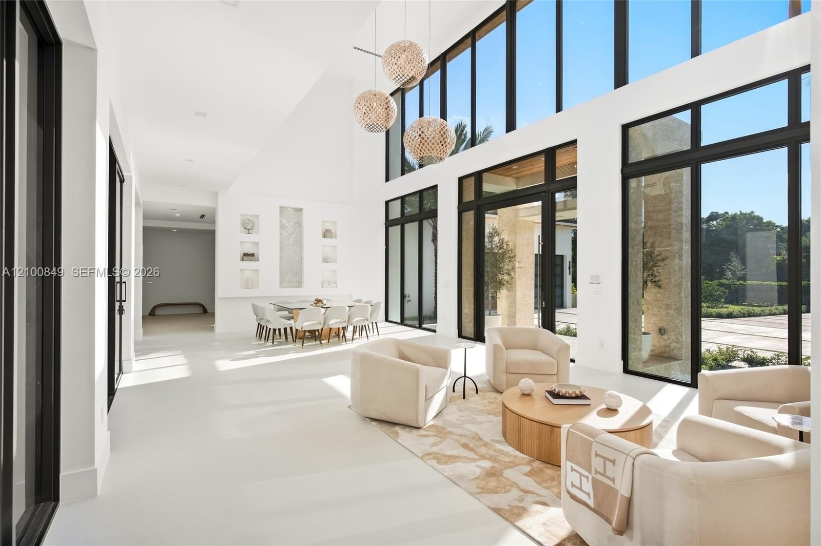 Expansive living area featuring vaulted ceilings, floor-to-ceiling windows with black frames, polished solid-surface flooring, and tiered multi-pendan