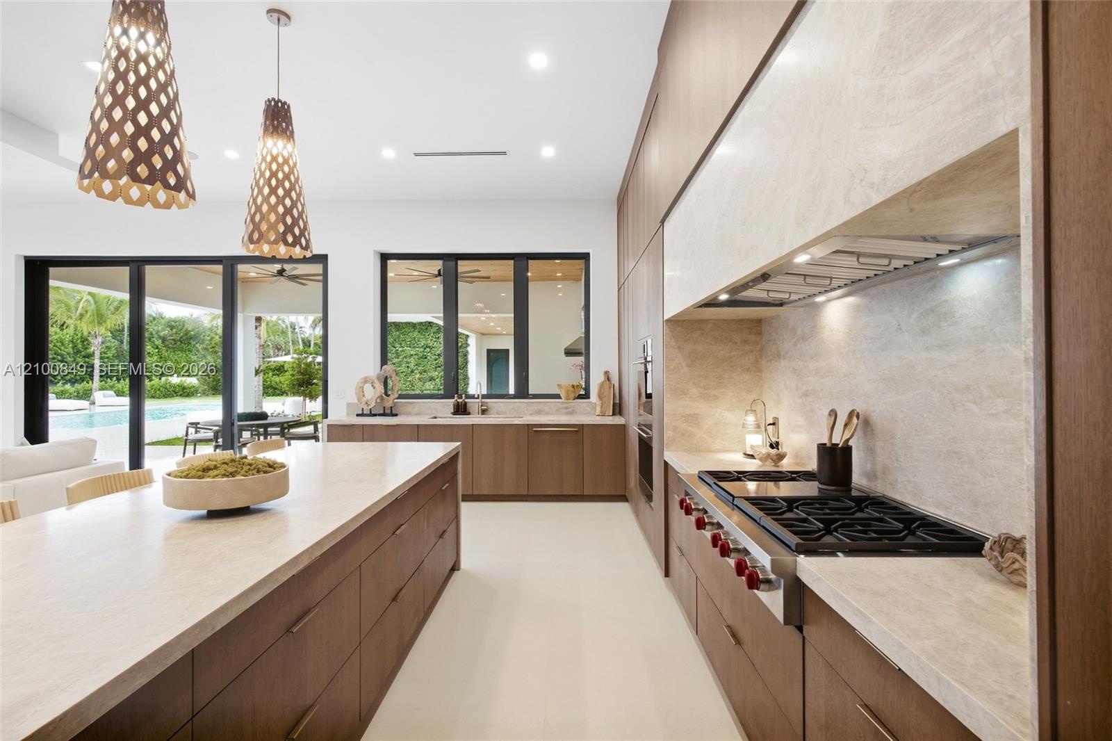 Modern kitchen featuring flat-panel wood cabinetry, a large central island with solid-surface countertops, professional-grade gas cooktop, and decorat