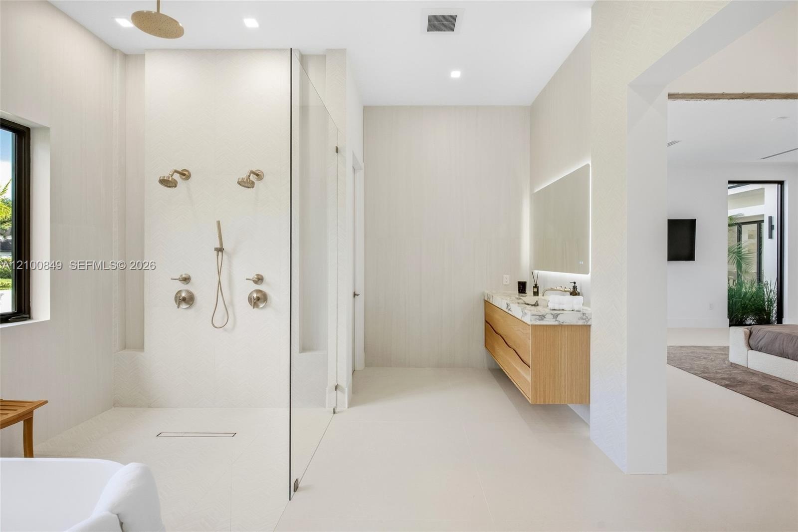 Walk-in shower featuring a glass enclosure, dual wall-mounted shower heads, a handheld sprayer, and ceiling-mounted rainfall head, accompanied by a fl