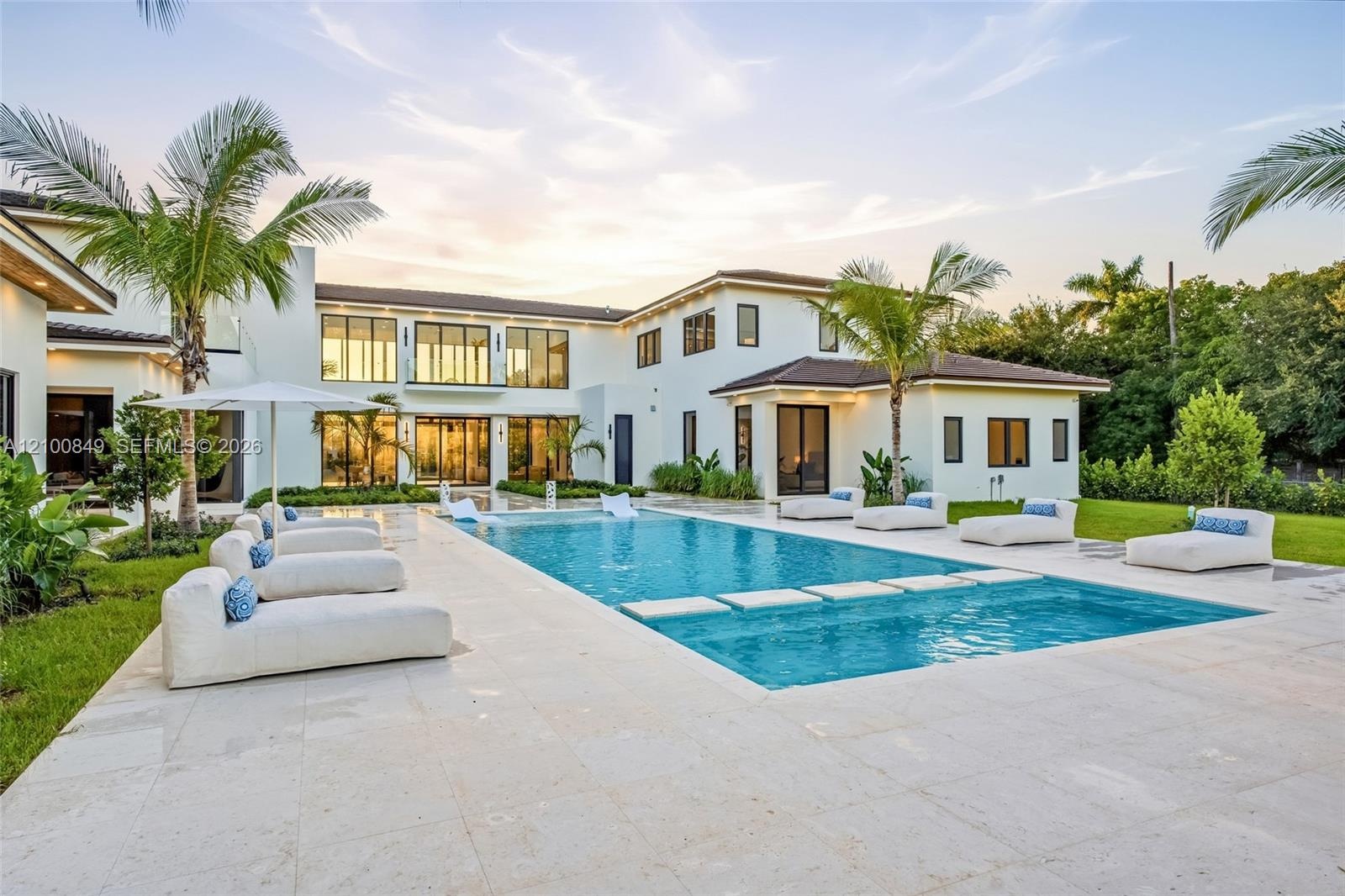 Two-story stucco exterior with a multi-level roofline, featuring a swimming pool with a built-in sun shelf, stone-paver pool deck, and integrated land