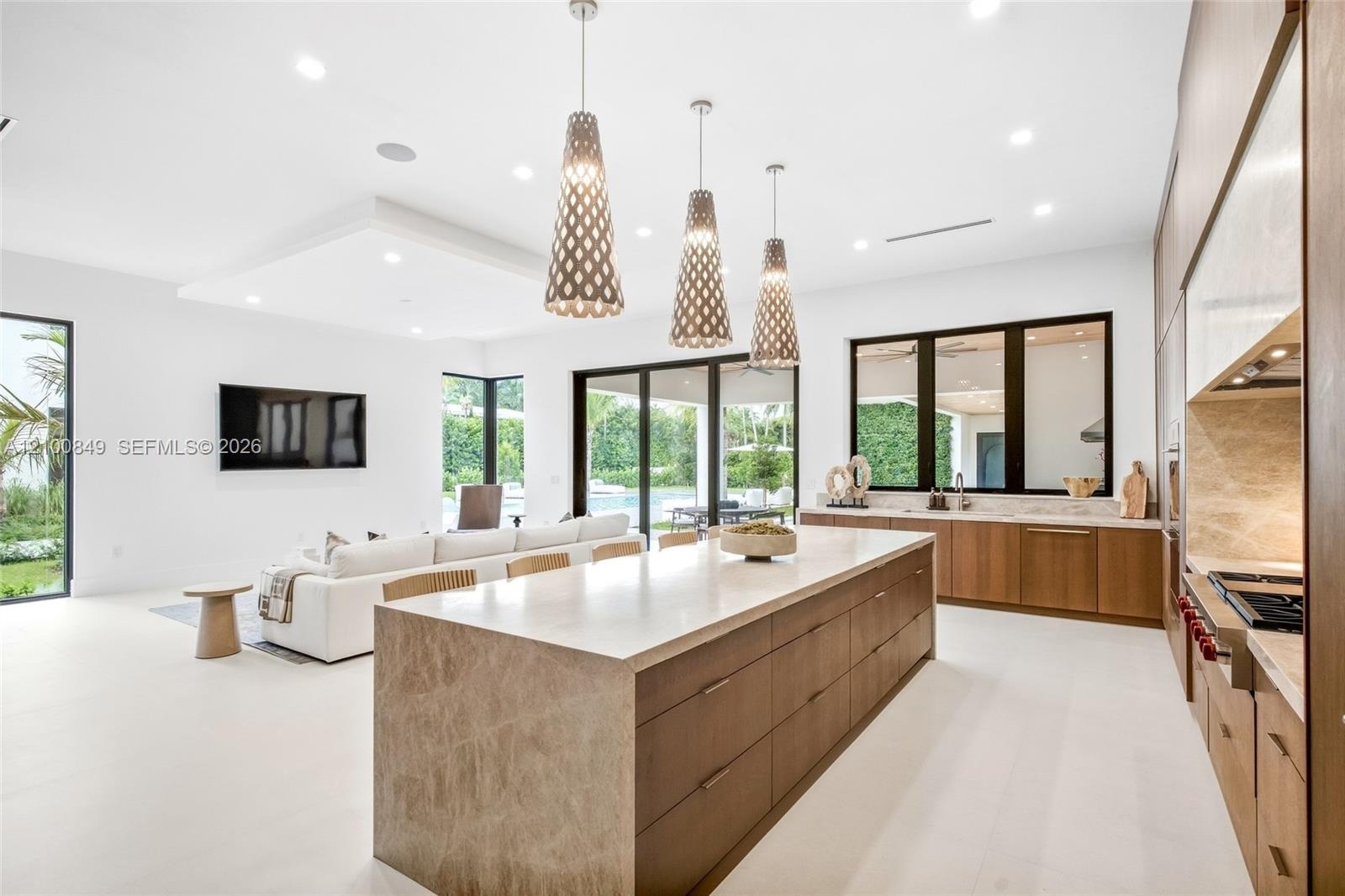 Chef's kitchen featuring a stone-topped waterfall island, custom wood cabinetry, recessed lighting, and trio of pendant light fixtures, finished with 