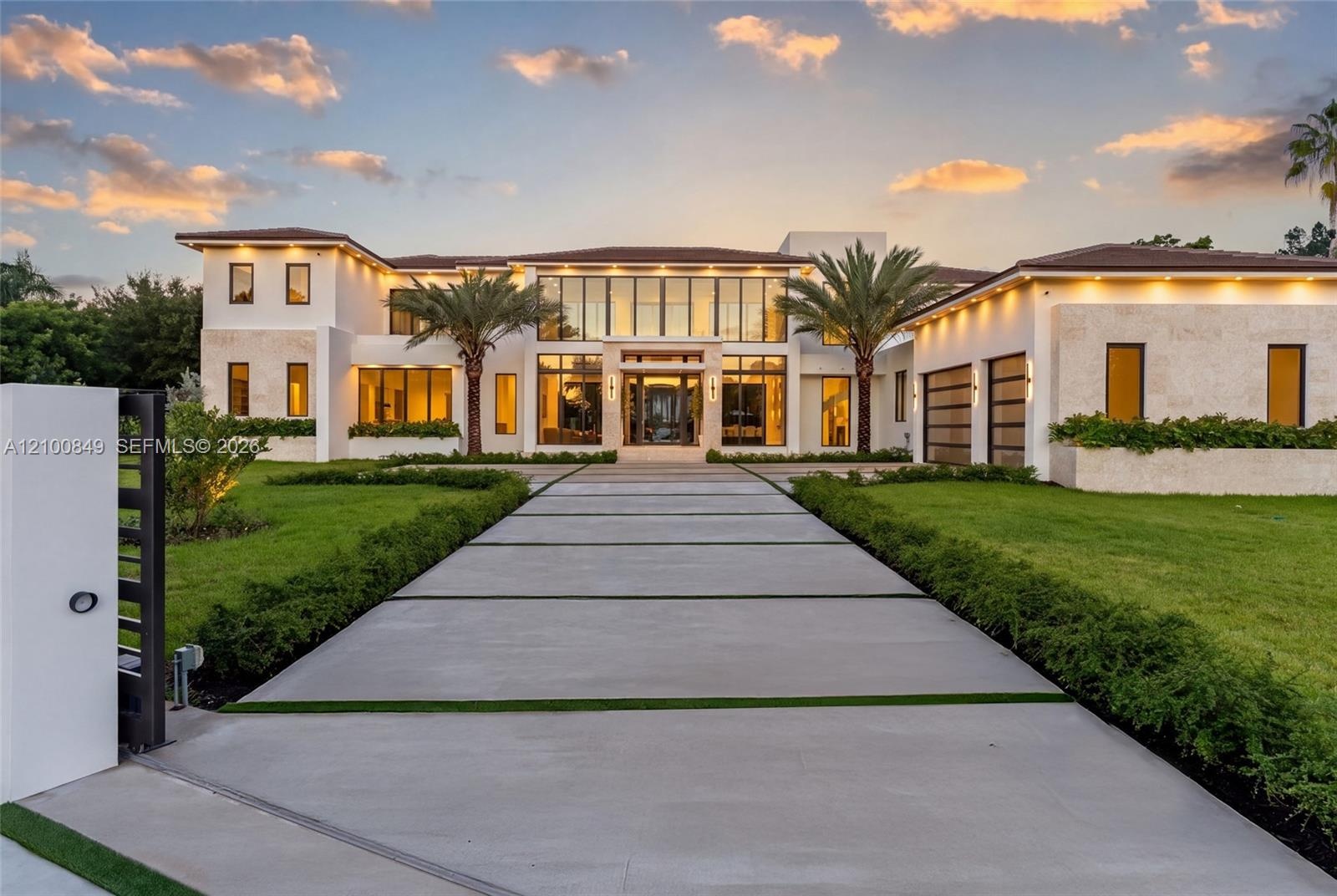 Contemporary two-story estate featuring a stone-clad exterior, floor-to-ceiling glass windows, a structured concrete paver driveway, and a gated entra