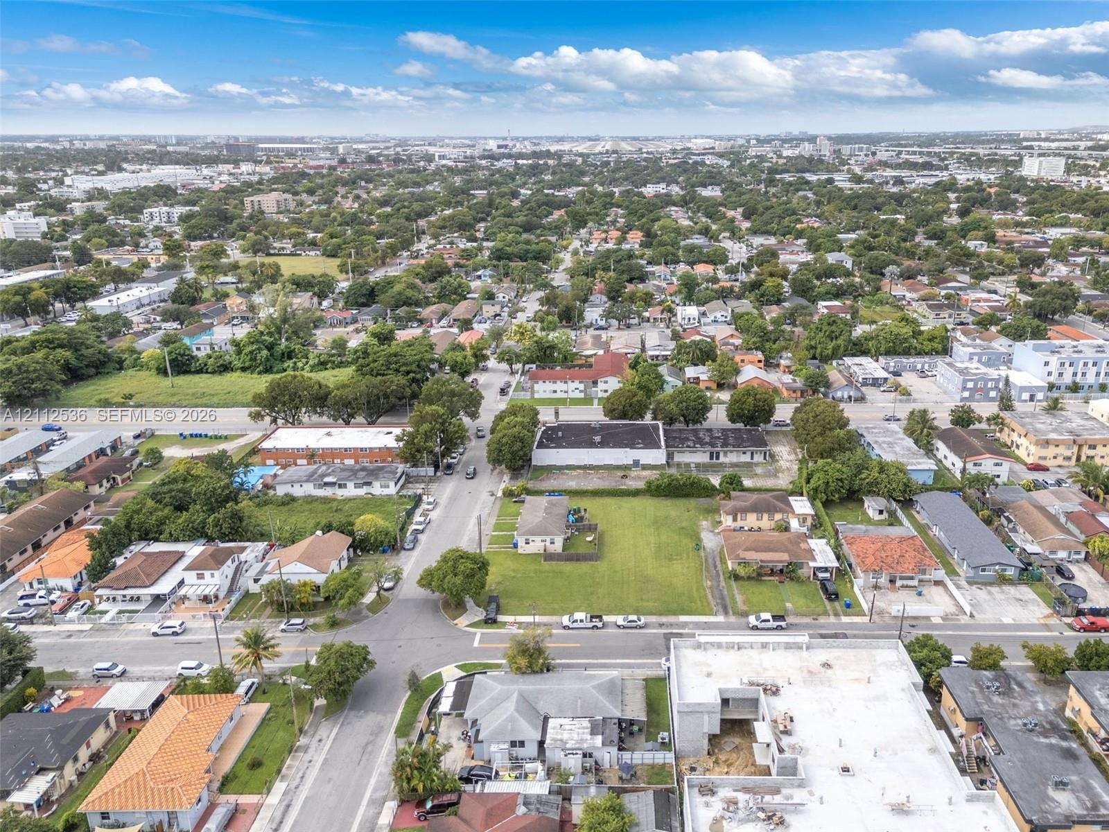 Aerial perspective of a corner lot featuring open, undeveloped green space, mature perimeter trees, and street-level access