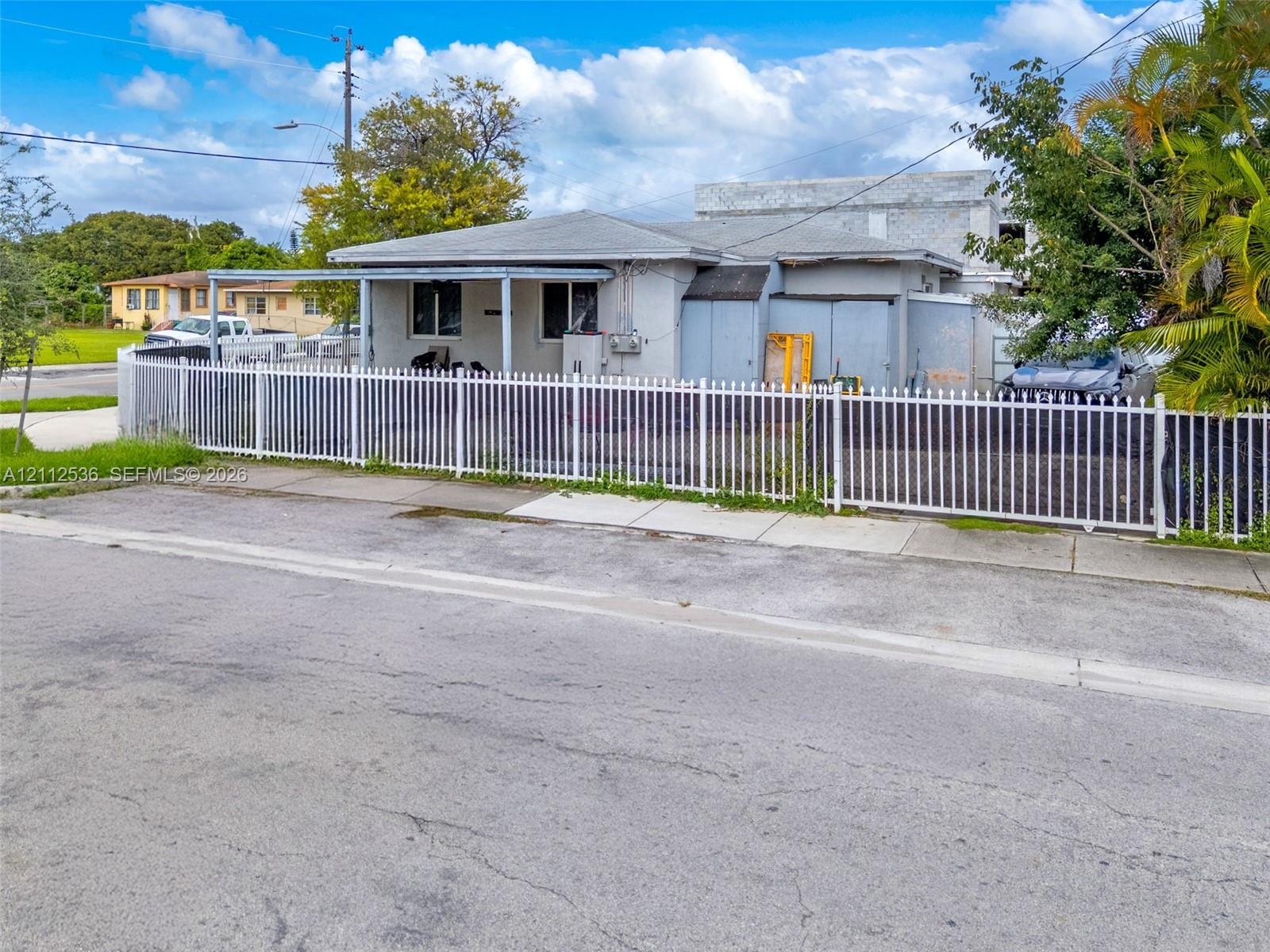 Single-story exterior featuring a covered front porch, light-toned stucco facade, and a full-perimeter metal fence