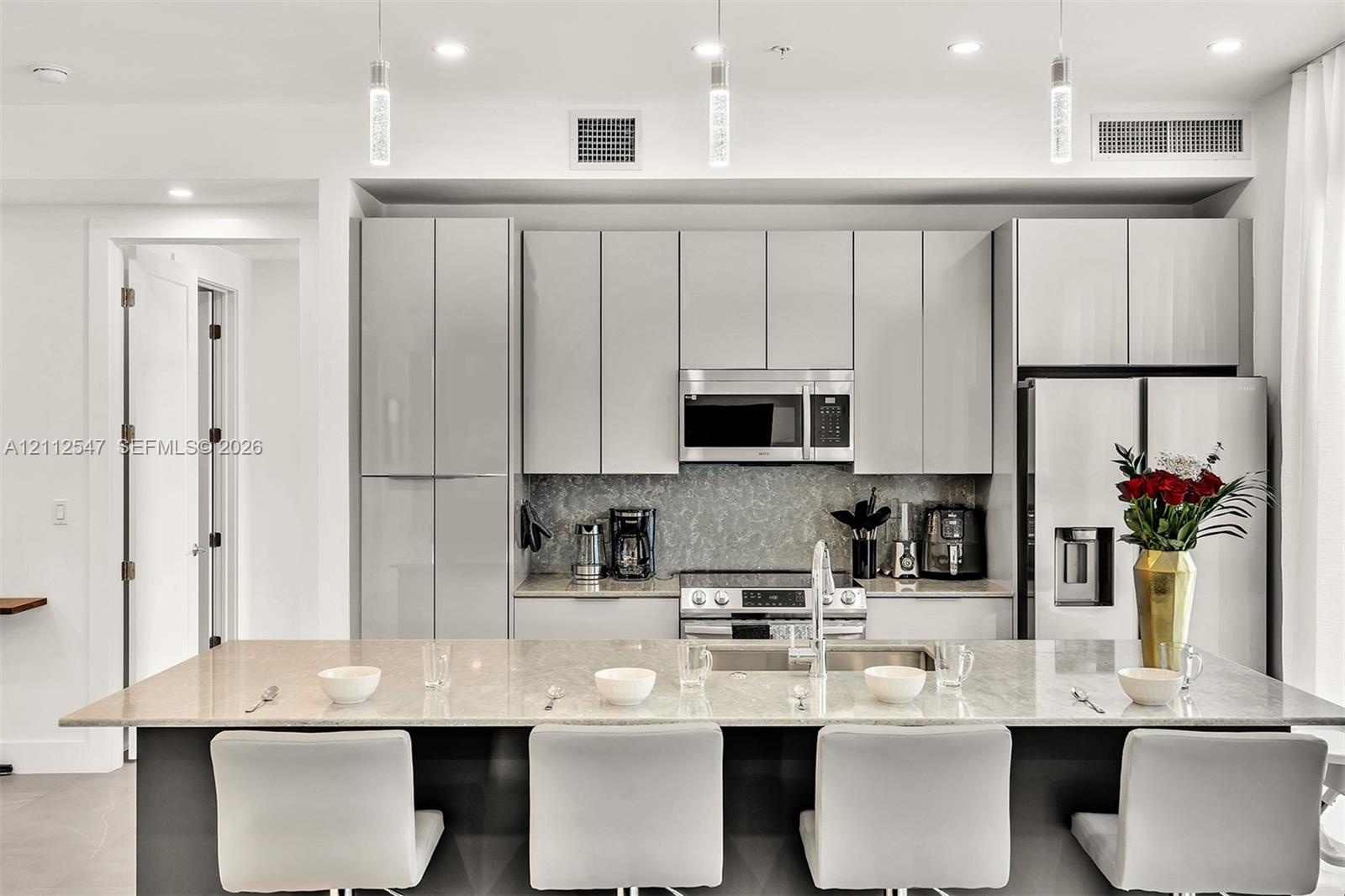 Kitchen featuring flat-panel cabinetry, a stone-surfaced kitchen island, stainless steel appliances, and glass pendant lighting