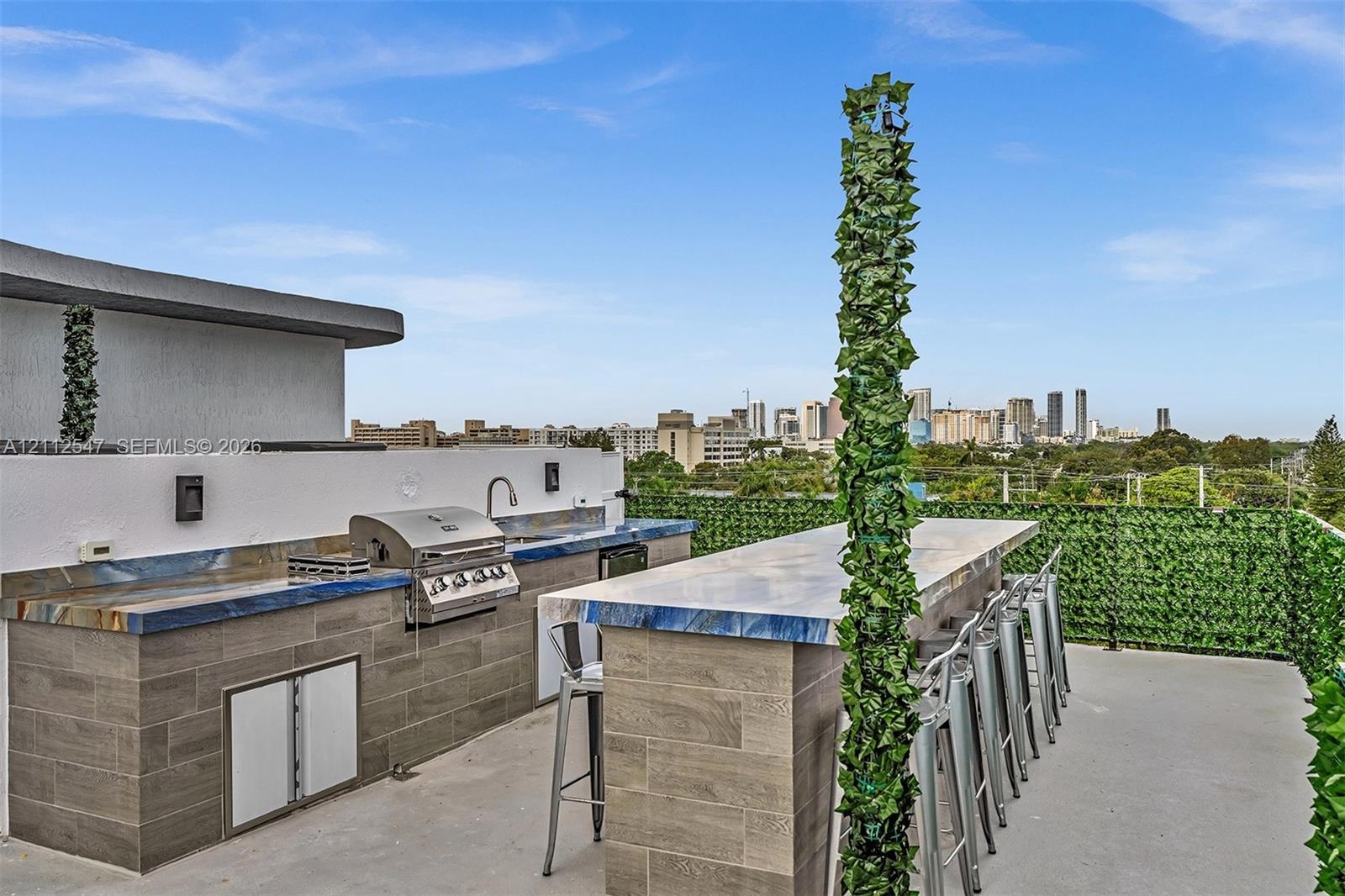 Rooftop terrace featuring a built-in outdoor kitchen with stainless steel grill, stone-finish countertops, tile-clad cabinetry, and an integrated bar 