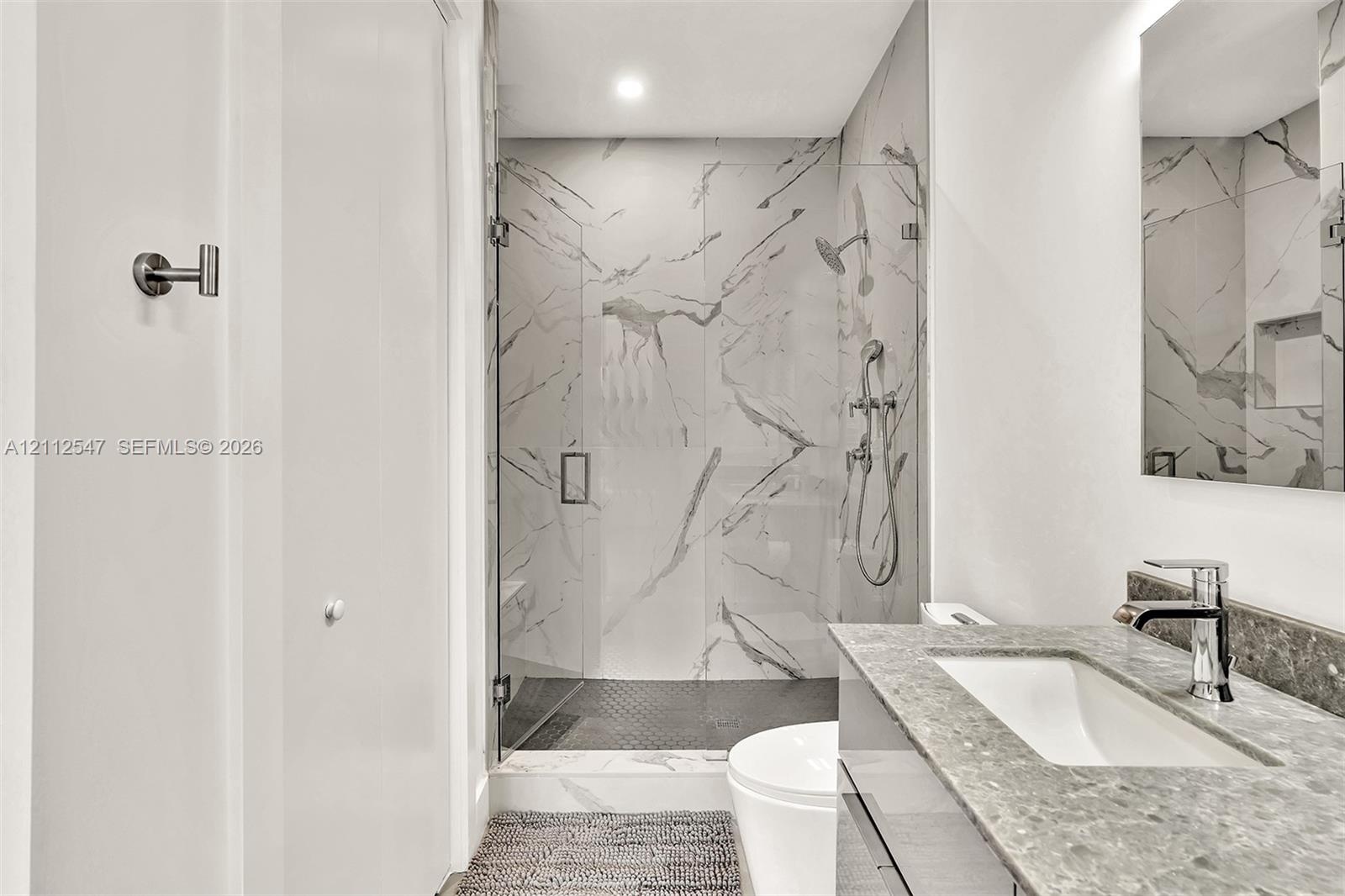 Bathroom featuring a walk-in shower with large-format stone-patterned tile, frameless glass enclosure, wall-mounted shower hardware, floating vanity w