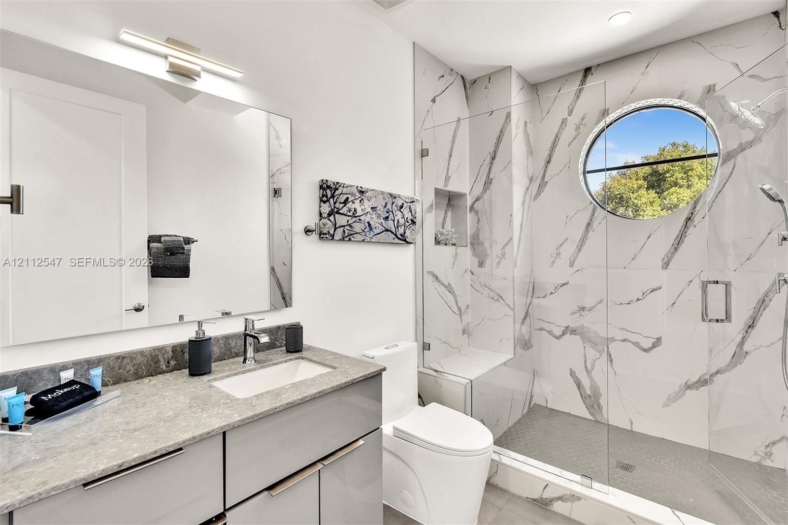 Bathroom featuring a sleek vanity with a stone countertop, an integrated rectangular sink, wall-to-wall mirror, walk-in shower with floor-to-ceiling s