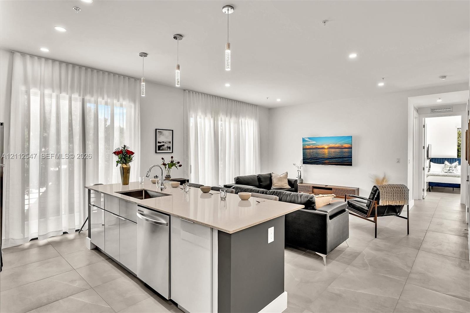Kitchen island featuring stone countertops, stainless steel undermount sink, and integrated stainless steel dishwasher, complemented by recessed light