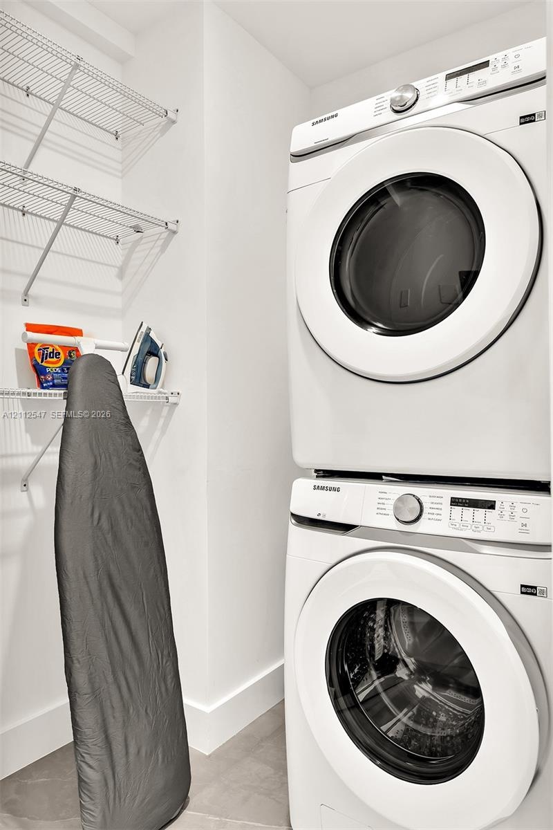 Laundry area featuring a stacked front-loading washer and dryer with integrated white wire shelving