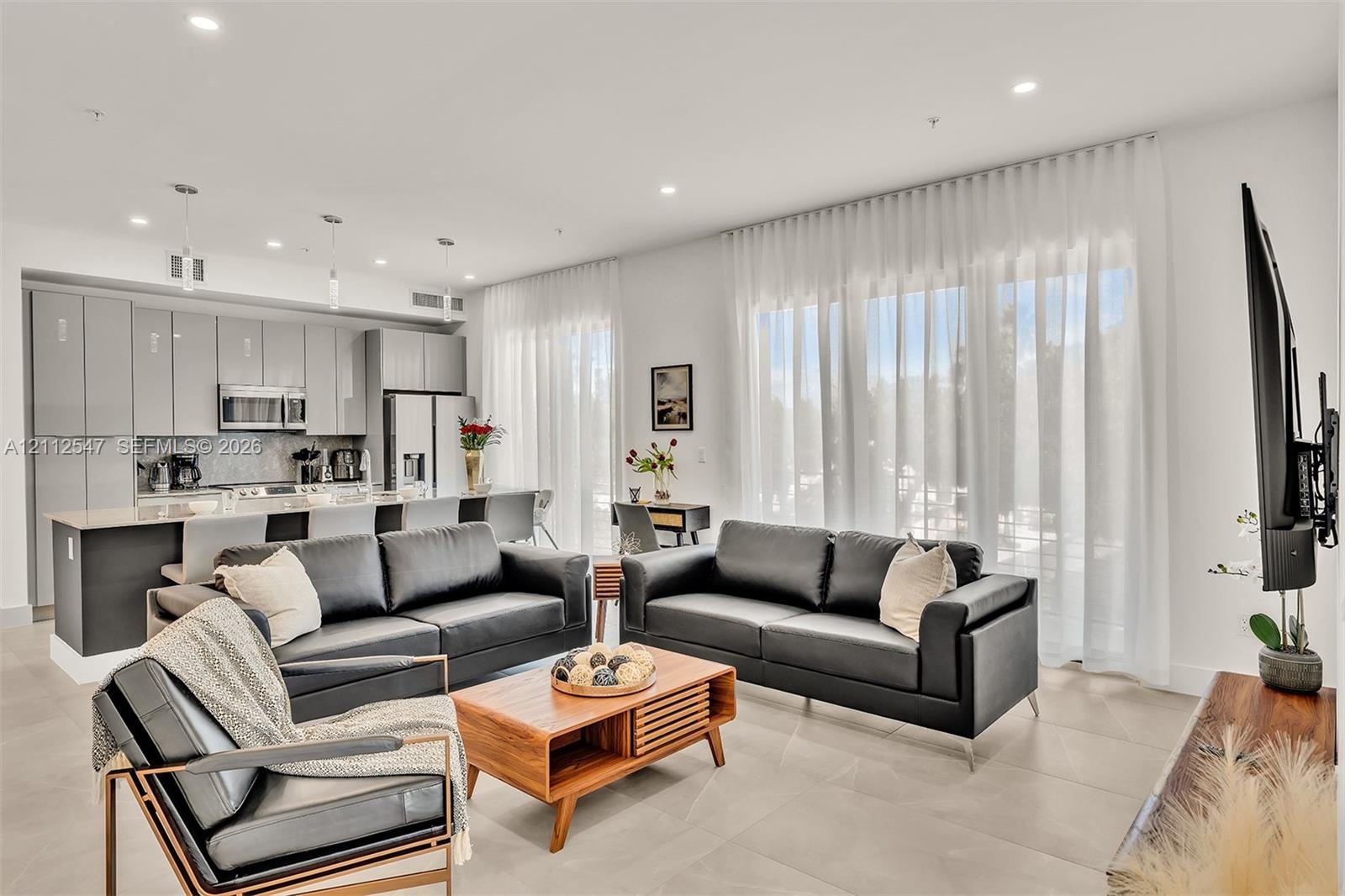 Open-concept interior featuring high-gloss cabinetry, stone-surface kitchen countertops, large-format tile flooring, and floor-to-ceiling windows with
