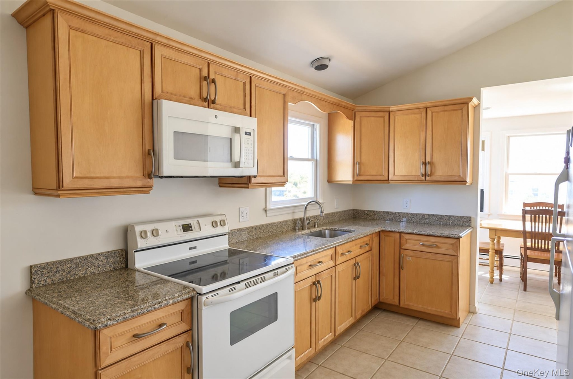 Kitchen featuring natural wood cabinetry, stone-finish countertops, tile flooring, and integrated white appliances