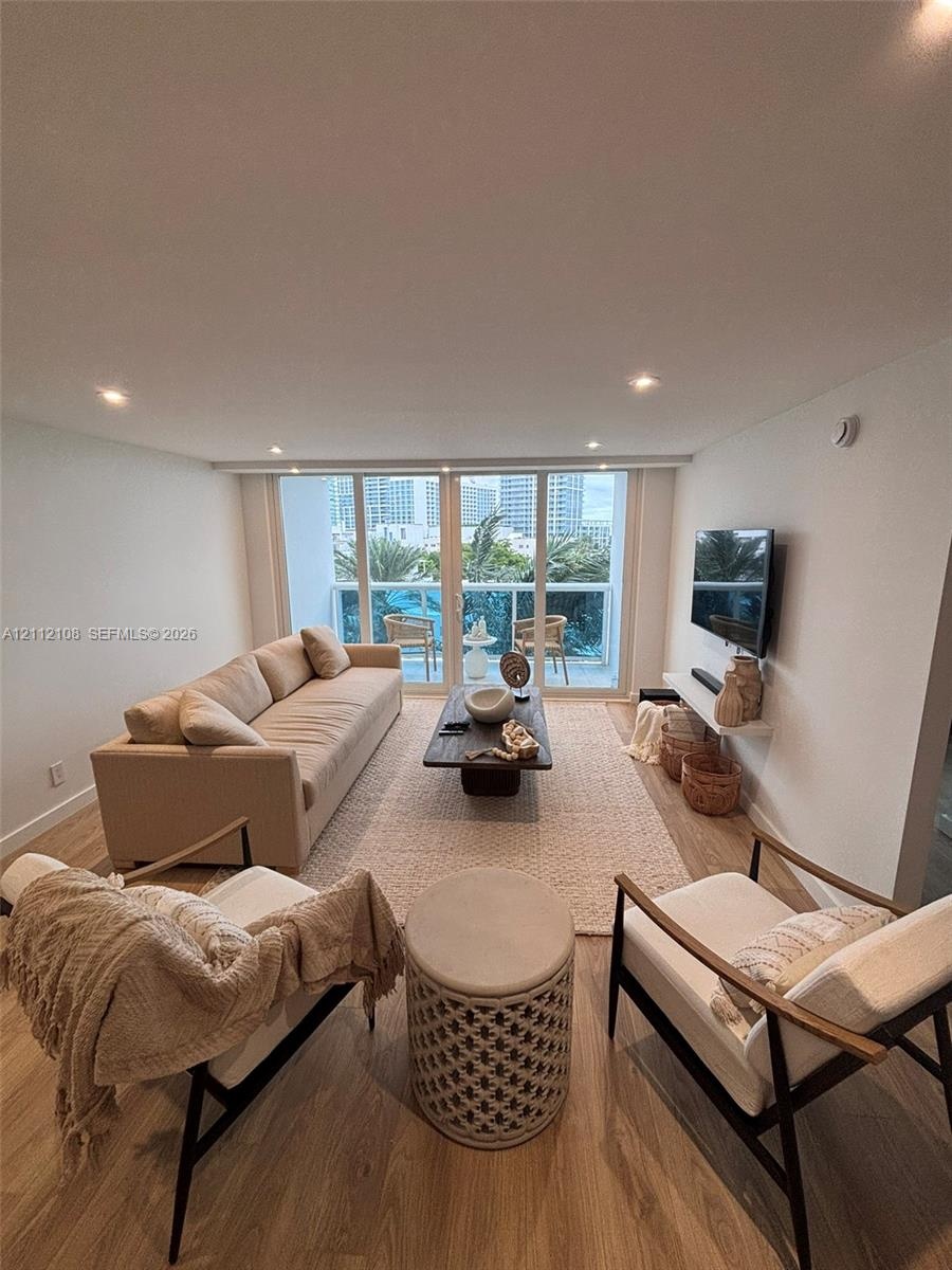 Living area featuring wood-finish flooring, recessed lighting, and floor-to-ceiling glass doors providing balcony access