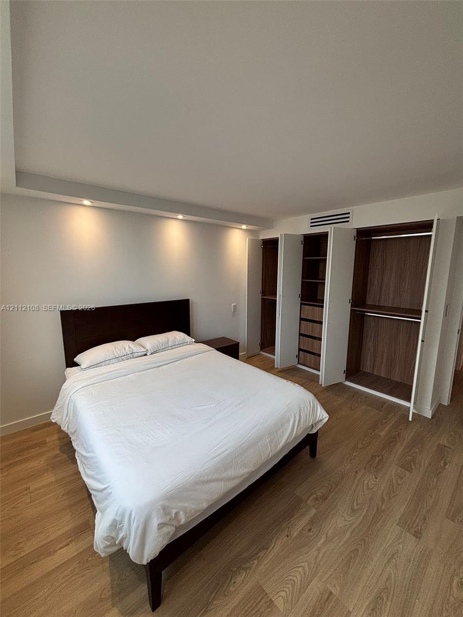 Wood-finish flooring, recessed ceiling lighting, and custom built-in cabinetry featuring integrated shelving, drawers, and hanging rods