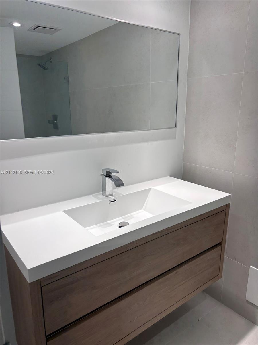 Floating vanity featuring a wood-finish cabinet with dual drawers, integrated white sink, polished chrome faucet, and large wall-mounted mirror agains