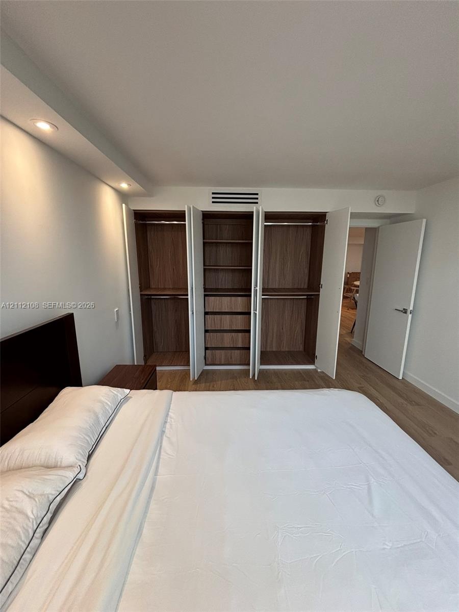 Built-in wardrobe system with wood-finish shelving and cabinetry, recessed ceiling lighting, and light-toned wood-finish flooring