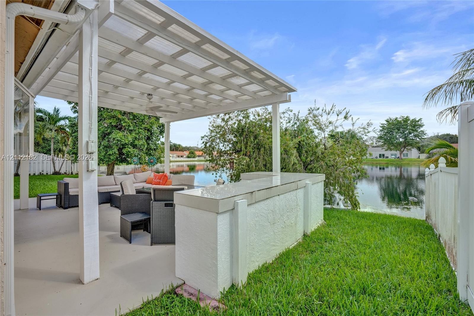 Covered patio featuring a white pergola, built-in concrete bar, concrete flooring, and water frontage