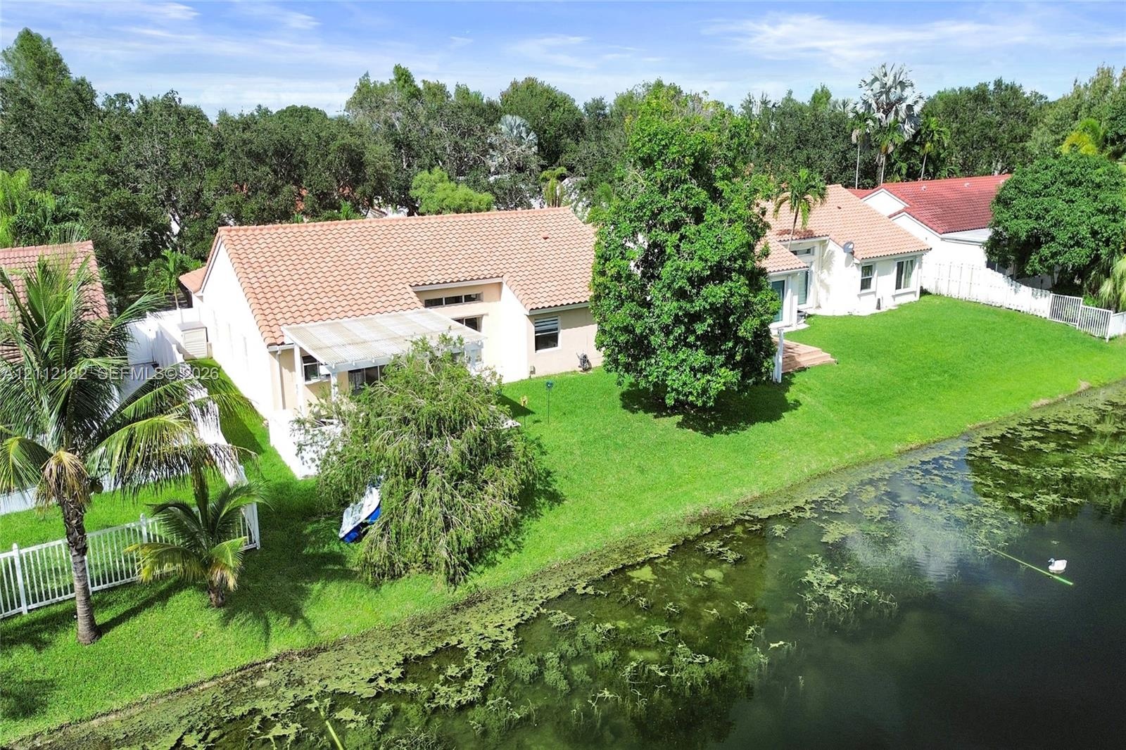 Waterfront property featuring a grass lawn, tile roof, and mature perimeter trees