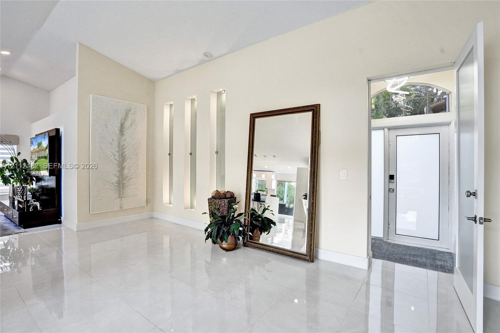 Entryway featuring large-format tile flooring, high vaulted ceilings, triple recessed wall niches, and a glass-paneled entry door with an arched trans