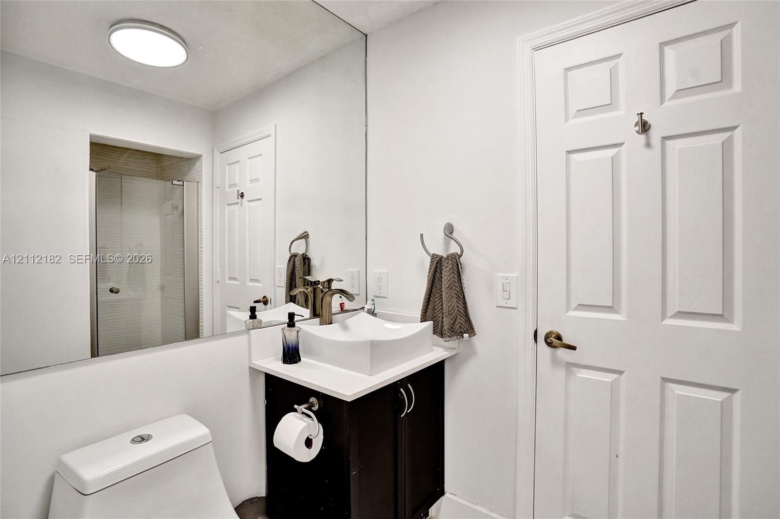 Vanity featuring a dark-finish base cabinet, solid-surface countertop, and white square vessel sink with a metallic faucet, complemented by a floor-to